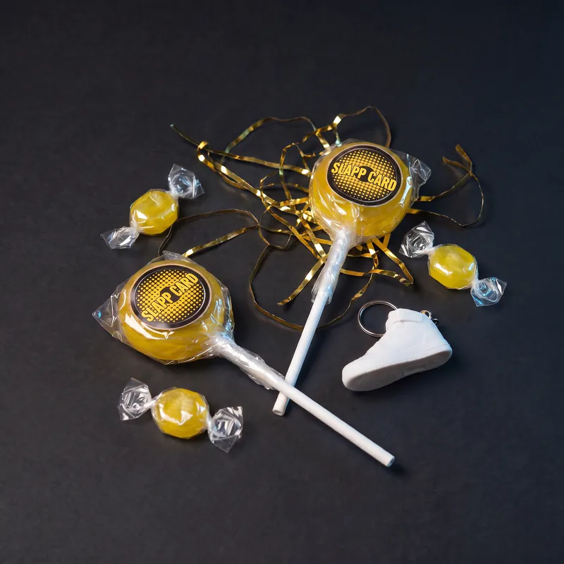 Two lollipops, three wrapped candies and a small white sneaker keychain among gold tinsel on a dark surface